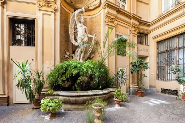 A courtyard with a central fountain, surrounded by potted plants and a classical statue. - Xenia Guest House (Rome)