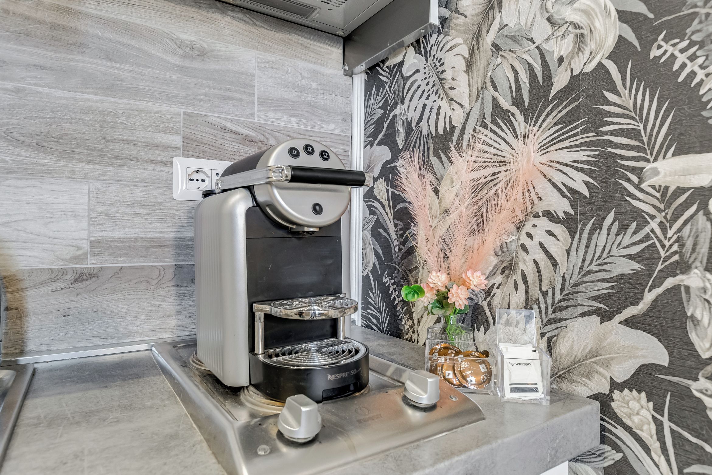 Una cocina moderna con una cafetera expreso integrada, una cafetera tradicional y un florero decorativo con flores.