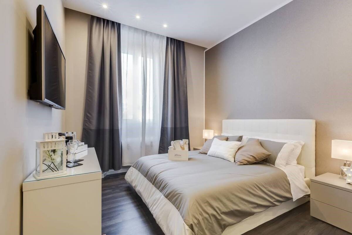 A hotel room with a bed, bedside tables, a TV, and a window with curtains.