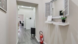 A hallway with a fire extinguisher, a small shelf with a plant, and a mirror on the wall. - Hanky Suite (Rome)