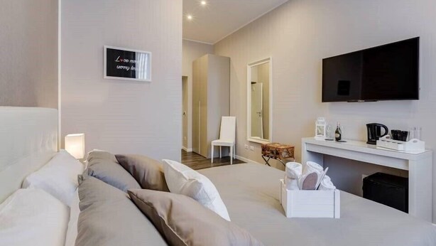 A modern hotel room with a bed, a TV, a desk with a coffee maker, and a mirror. - Hanky Suite (Rome)