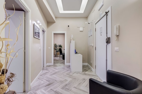 A hallway with a modern design, featuring a herringbone floor pattern, a reception desk, and a seating area with a chair.