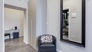 A modern room with a dark armchair, a large mirror, and a small desk with a coffee machine. - Hanky Suite (Rome)