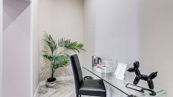A modern room with a glass table, a black chair, a potted plant, a kettle, and a welcome sign.