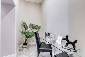 Une chambre moderne avec une table en verre, une chaise noire, une plante en pot, une bouilloire et un panneau d’accueil.