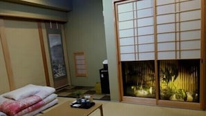 A traditional Japanese room with tatami flooring, a low table, a futon bed, and a shoji screen with a fish tank.