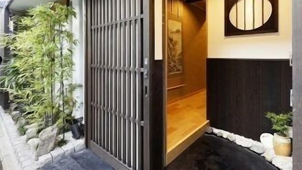 A traditional Japanese entrance with a sliding door, a small garden area with rocks and plants, and a wall-mounted decorative panel.