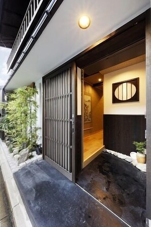 A traditional Japanese entrance with a sliding door, a small garden area with rocks and plants, and a wall-mounted decorative panel. - Kyoto Himawari Shijo Kawaramachi (Kyoto)