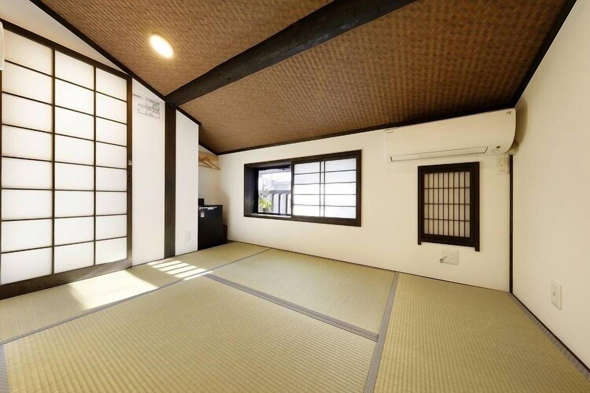 A traditional Japanese room with tatami flooring, shoji screens, and a window with a view.