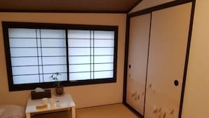 A traditional Japanese room with tatami flooring, a shoji screen window, a small table with a plant, and a sliding door with paper cut-out designs.