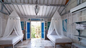 Quarto com duas camas, cada uma com dossel, um banco de madeira e vista para o verde lá fora.