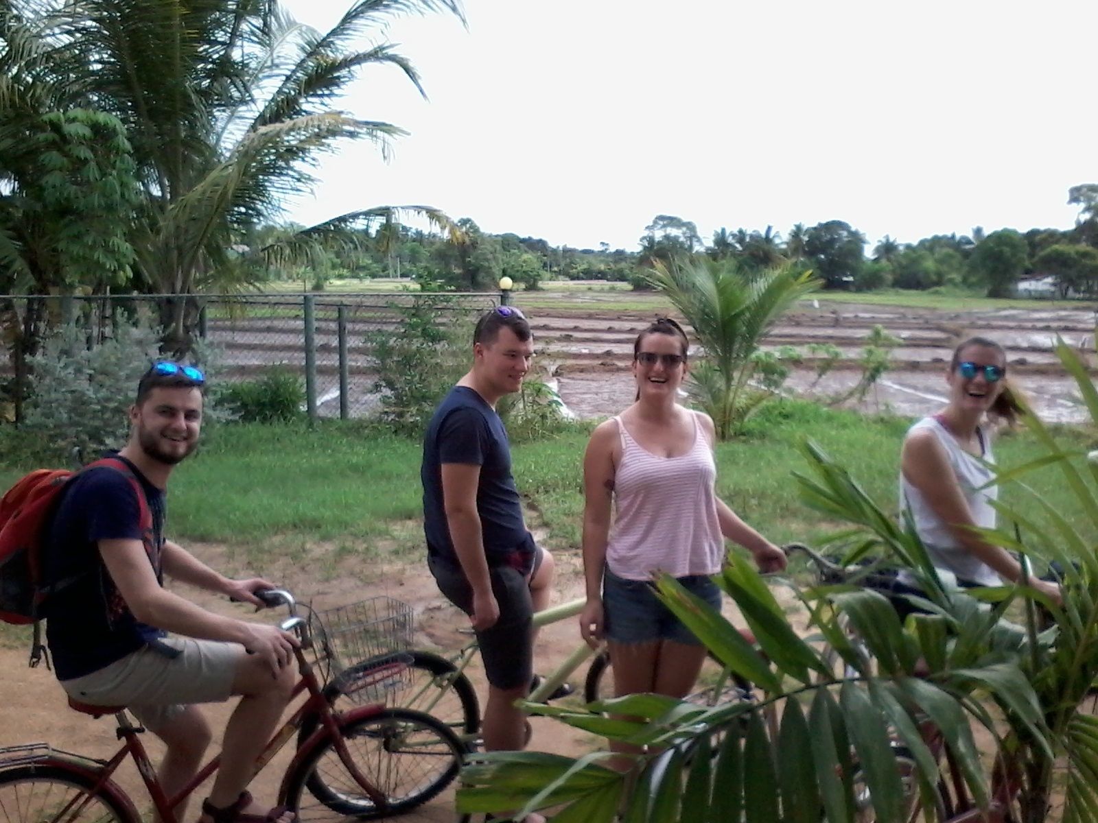 Un grupo de personas cerca de una bicicleta, con un paisaje rural y palmeras al fondo.