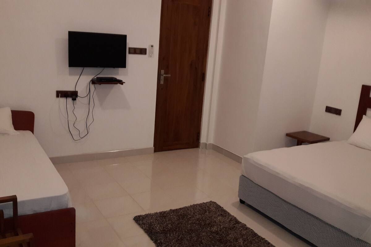 A hotel room with two beds, a flat-screen TV mounted on the wall, a wooden door, and a small bedside table.