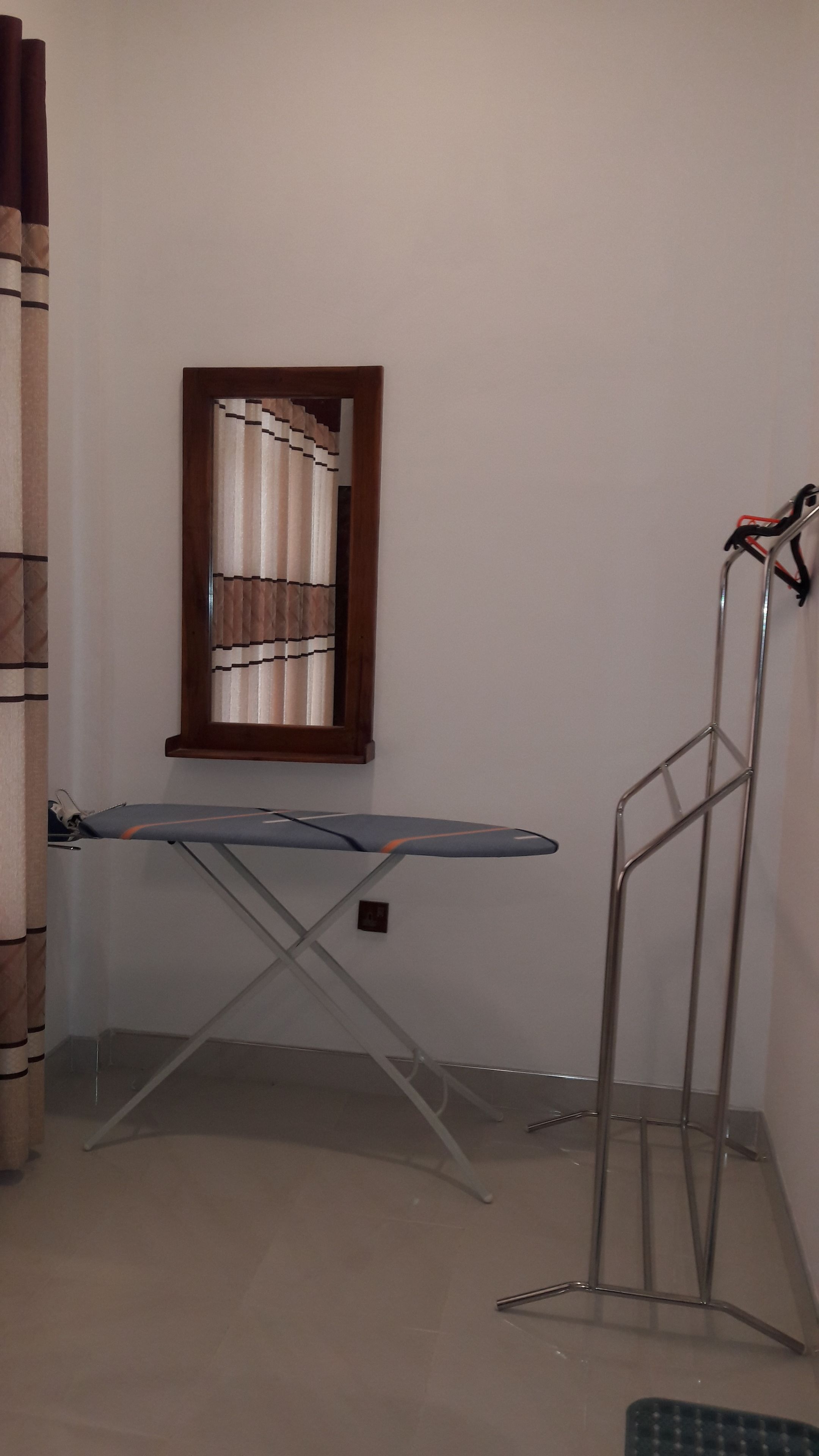A room with a wooden-framed mirror, a metal ironing board, and a metal drying rack.