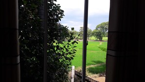 A view through a window with a view of a green field and trees. - Risenlak Holiday Resort (Polonnaruwa)
