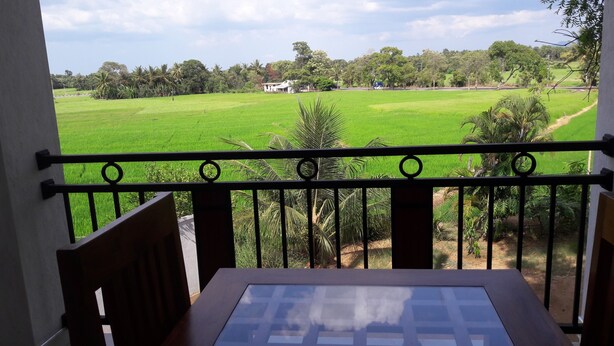 A balcony with a view of a green field and trees. - Risenlak Holiday Resort (Polonnaruwa)