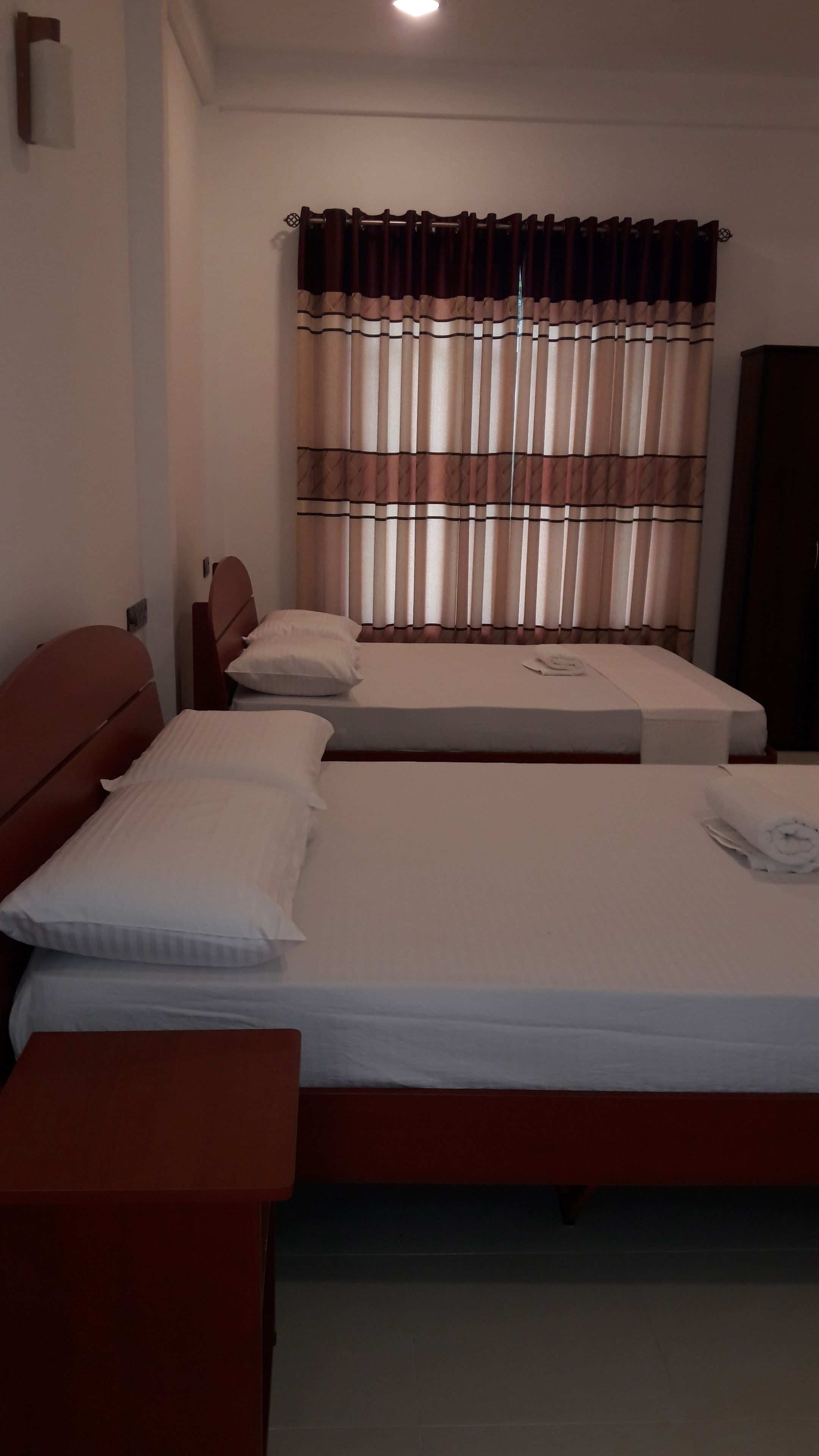 A hotel room with two beds, a wooden headboard, a nightstand, and a wardrobe.