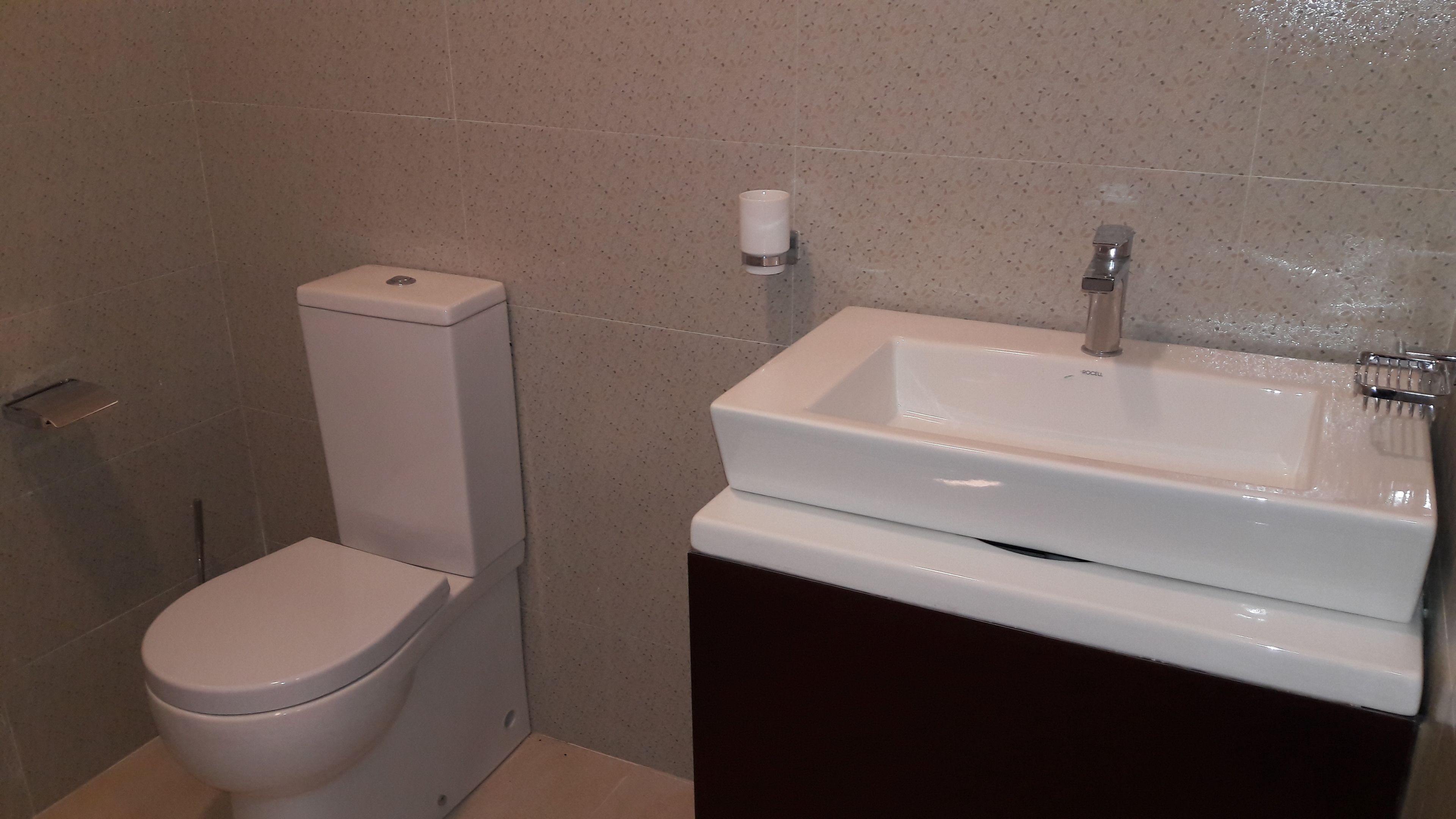 Une salle de bain équipée de toilettes, d’un lavabo et d’un porte-rouleau de papier toilette fixé au mur.