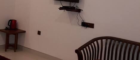 A living room with a flat-screen TV mounted on the wall, a wooden coffee table, a striped chair, and a small side table with a red object on it.
