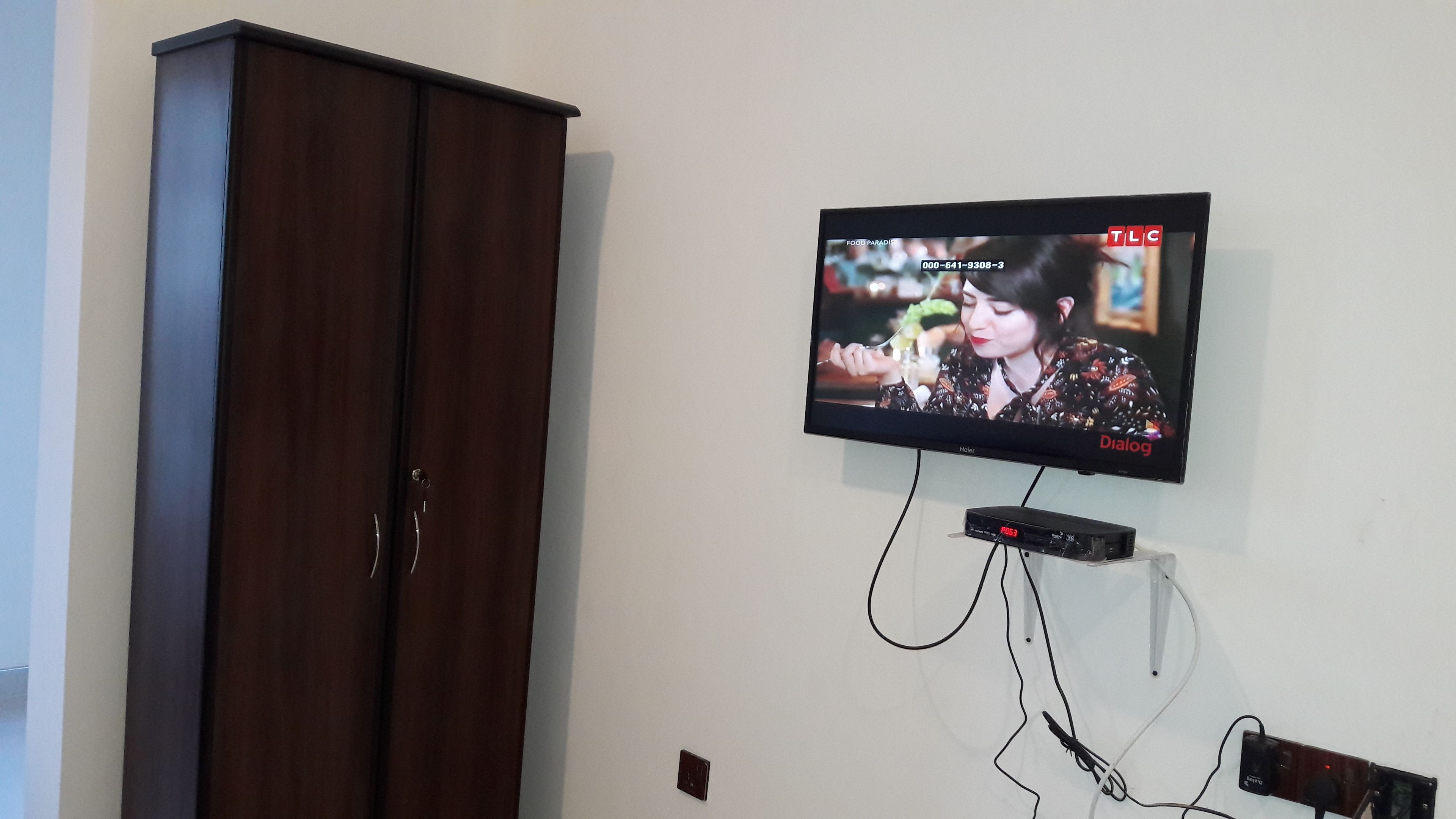 Un televisor montado en la pared, con un armario de madera a la izquierda.
