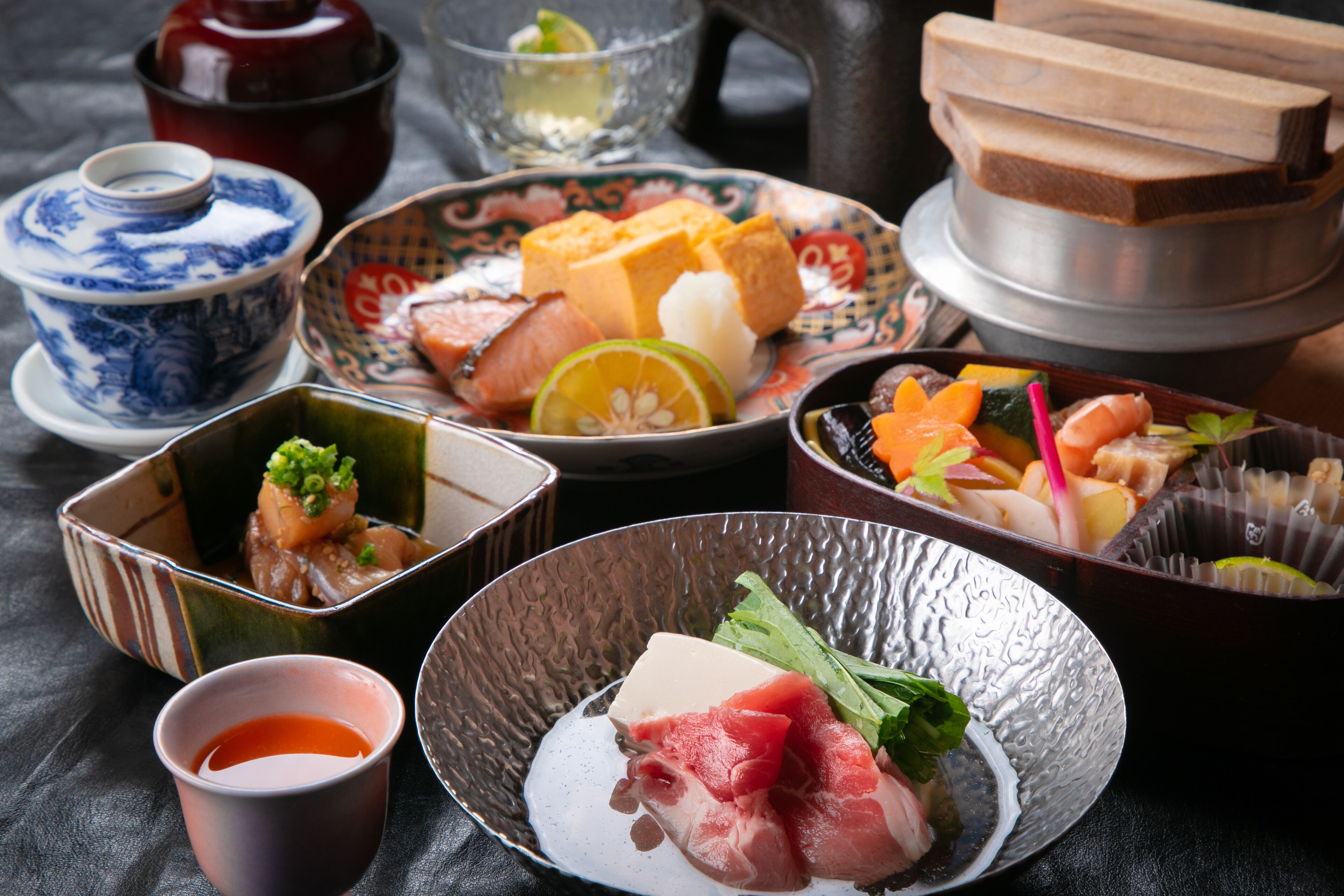 Una mesa con diferentes platos, como sushi, sashimi y un tazón de sopa.