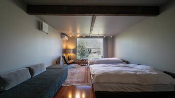 Een moderne slaapkamer met een groot bed, een sofa, een klein tafeltje en een raam met uitzicht op de omgeving.