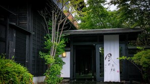 En traditionel japansk bygning med mørkt træfacade, flisetag og et hvidt banner med kalligrafi.