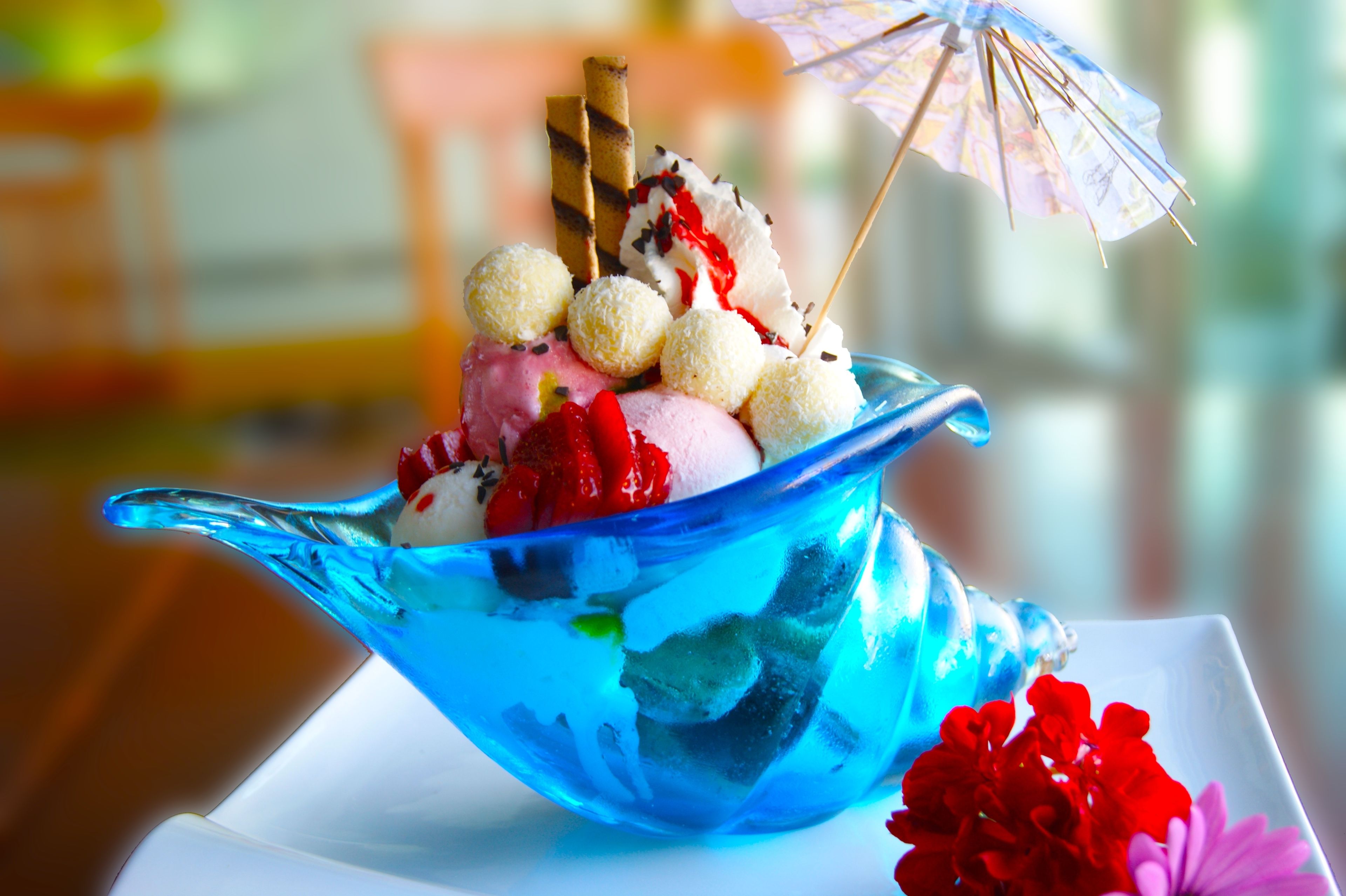 A dessert in a blue glass bowl with various toppings, including a small umbrella.