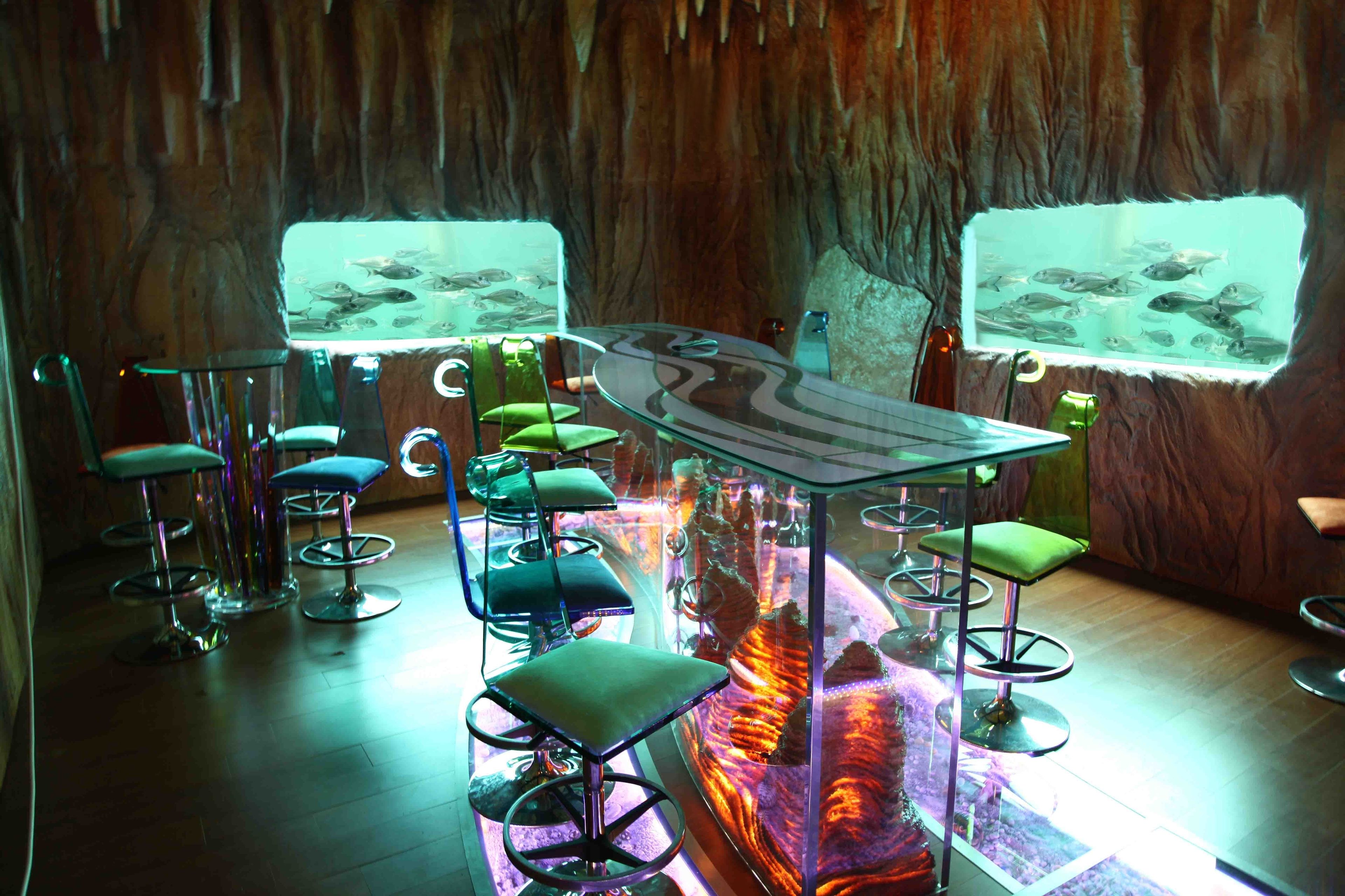 A bar area with multiple stools and a central table, surrounded by aquarium walls.