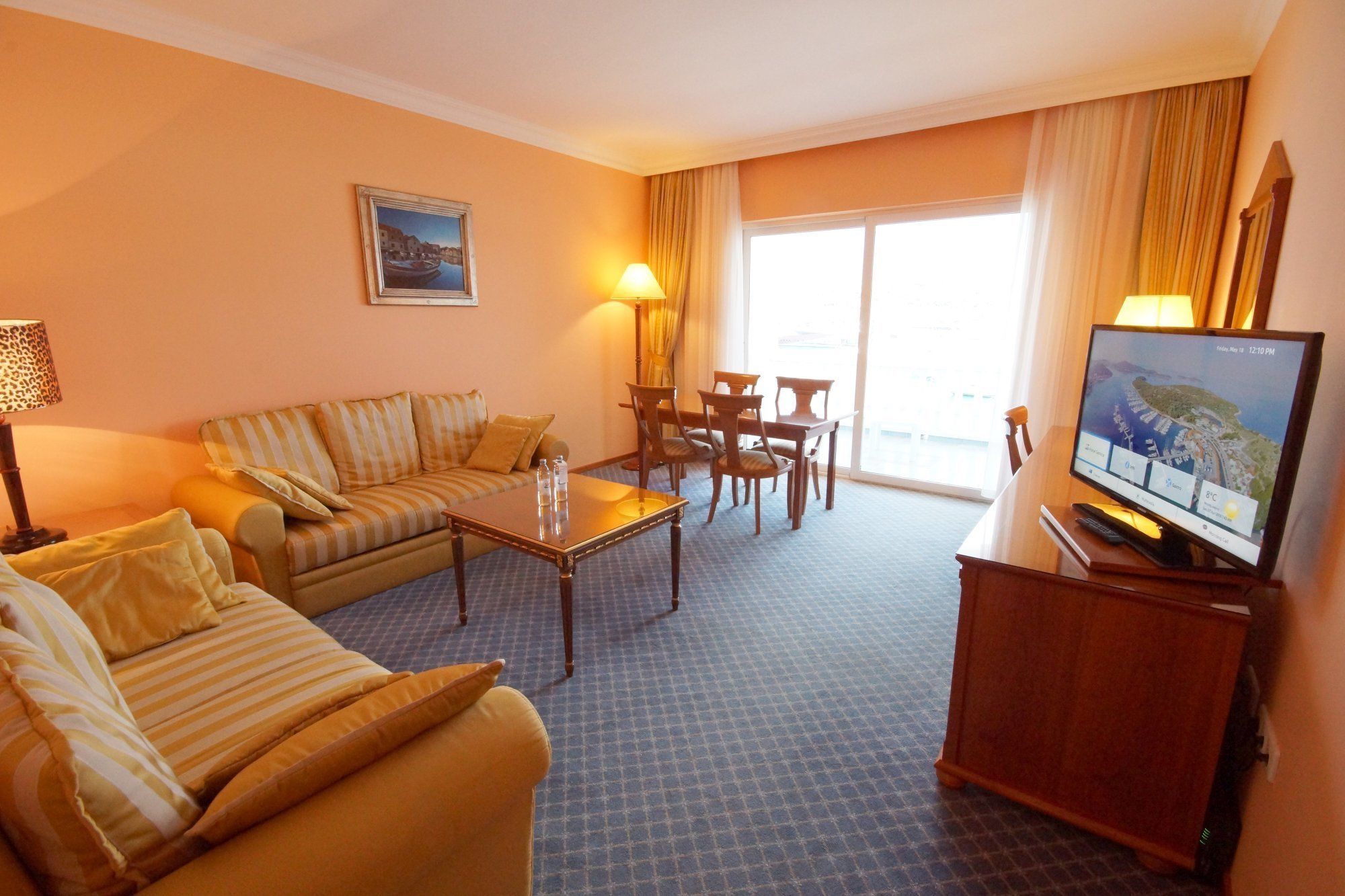 A hotel room with a sofa, a coffee table, a TV, and a dining area with chairs and a table.