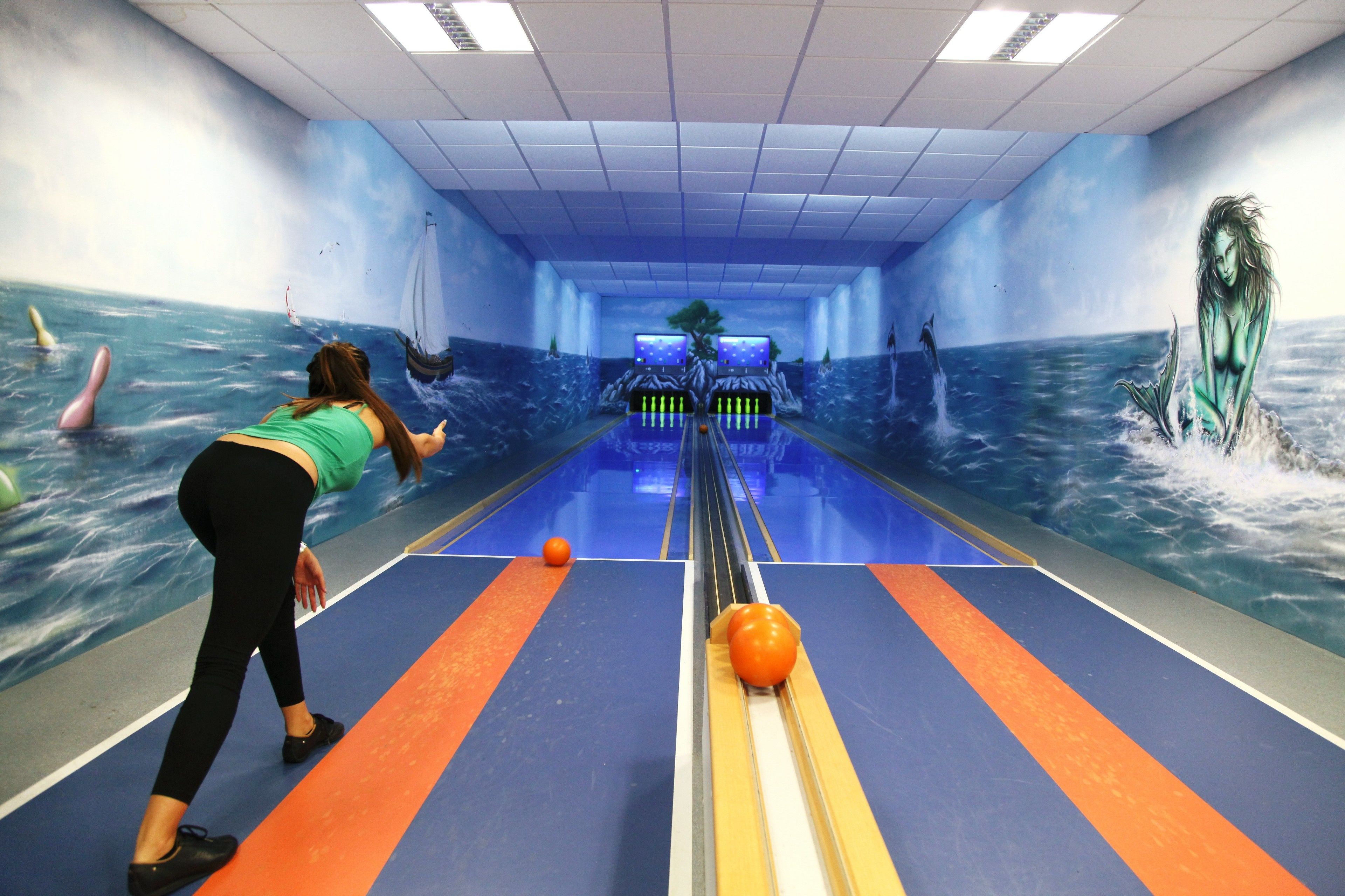 A bowling alley with a mural of ocean scenes on the walls.