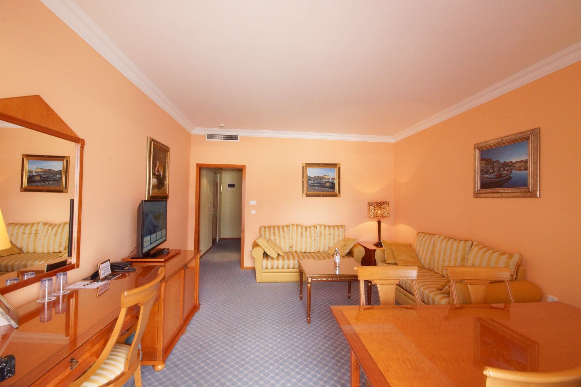 Una habitación de hotel con un escritorio de madera, un televisor, un sofá a rayas, una mesita y un espejo.