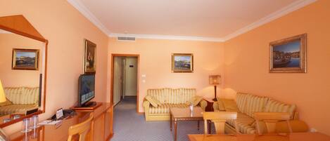 A hotel room with a wooden desk, a television, a striped sofa, a small table, and a mirror.