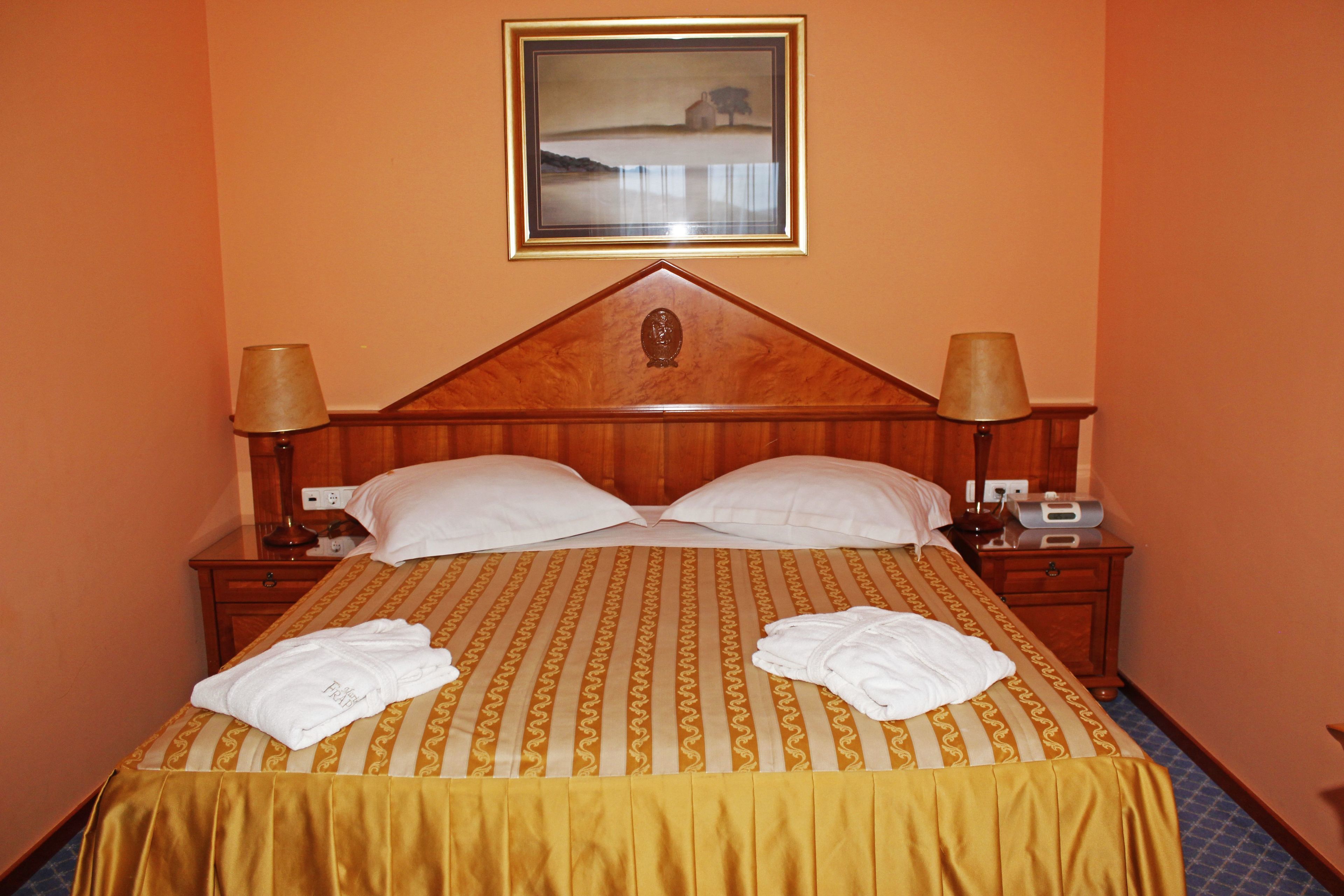 Een hotelkamer met een groot bed, twee nachtkastjes, een lamp en een lijst met foto aan de muur.