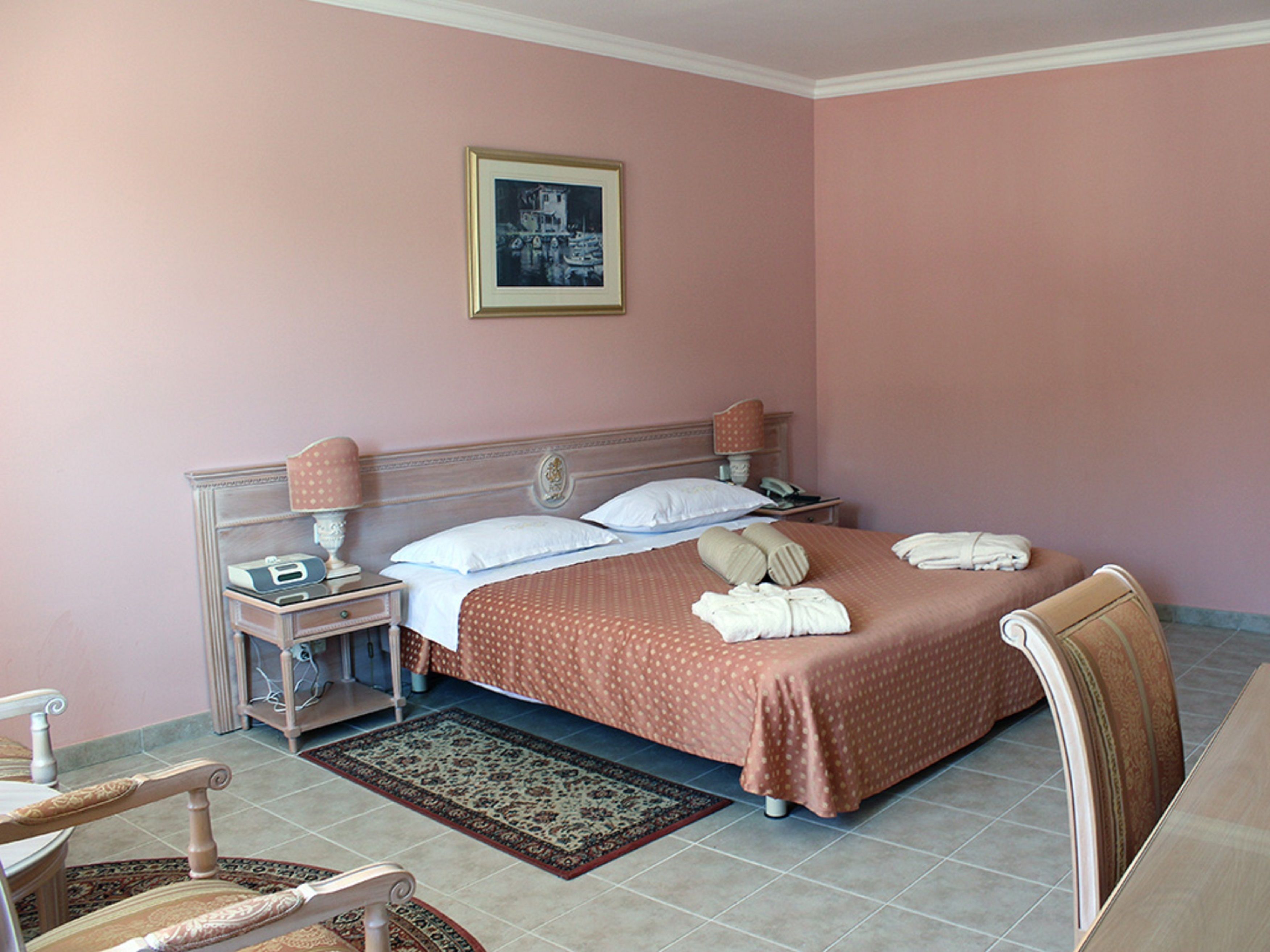 A hotel room with a bed, bedside tables, a chair, a rug, and a framed picture on the wall.