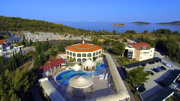 An aerial view of a resort with a swimming pool, a covered area, and a parking lot.