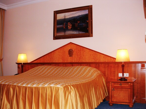 Un cuarto de hotel con cabecera de madera, una cama con cubrecama a rayas, dos lámparas de noche, una mesita de noche y un cuadro en la pared.