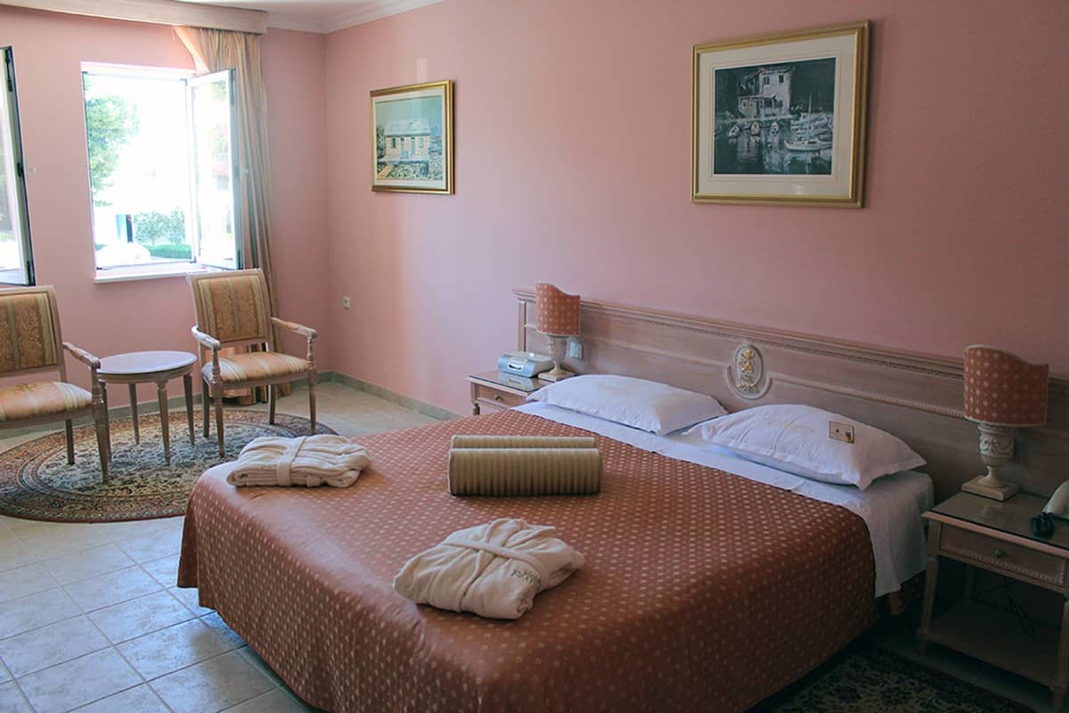 Ein Hotelzimmer mit einem großen Bett, zwei Stühlen, einem Nachttisch und einem Fenster mit Vorhängen.
