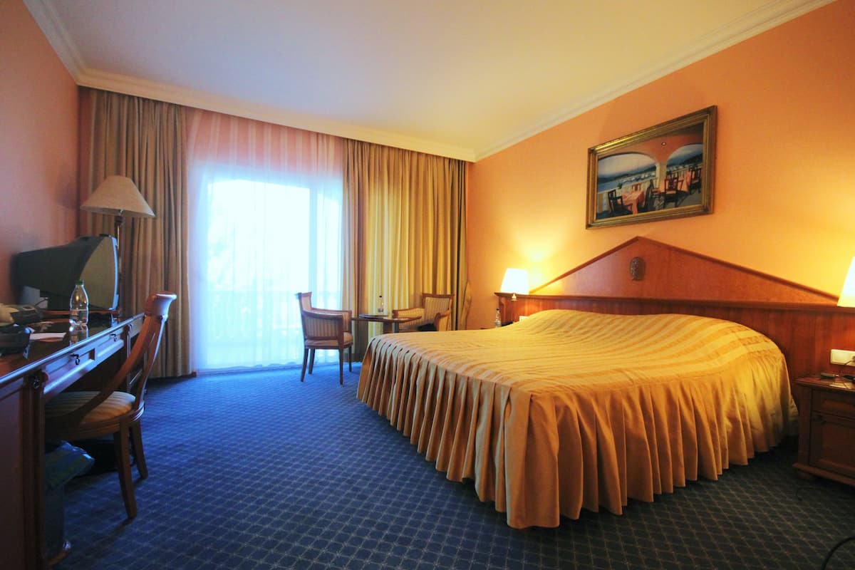 Ein Hotelzimmer mit einem großen Bett, einem Schreibtisch mit Stuhl, einer Lampe und einem Bild an der Wand.