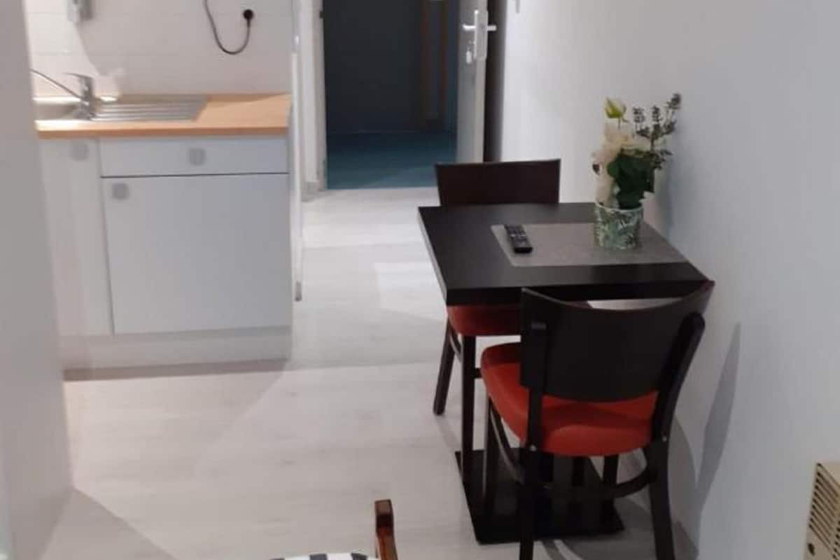 Une chambre d’hôtel compacte dotée d’une kitchenette, d’un coin repas avec une table et des chaises, et d’un lit avec une literie à rayures.