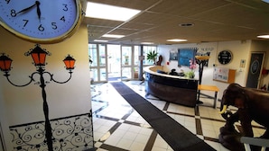 En receptionsområde med et ur, en receptionsdisk, en dekorativ lampe og et vægur.