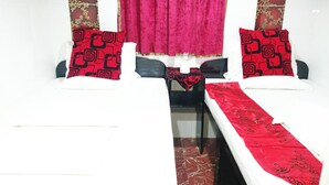 Une chambre avec deux lits, chacun agrémenté d’un coussin à motifs rouges et d’une couverture blanche. Une petite table recouverte d’une nappe rouge se trouve entre les deux lits, et une fenêtre est ornée d’un rideau rouge.