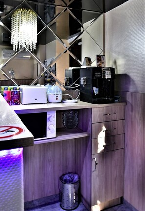 A compact kitchen with a coffee maker, a microwave, and a small refrigerator. There is a trash bin and a wooden cabinet with drawers. - EXPO Hotel Comfort (Kyiv)