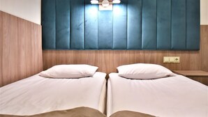 A double bed with white bedding and two pillows, a wooden headboard, and a small bedside table with a lamp. - EXPO Hotel Comfort (Kyiv)