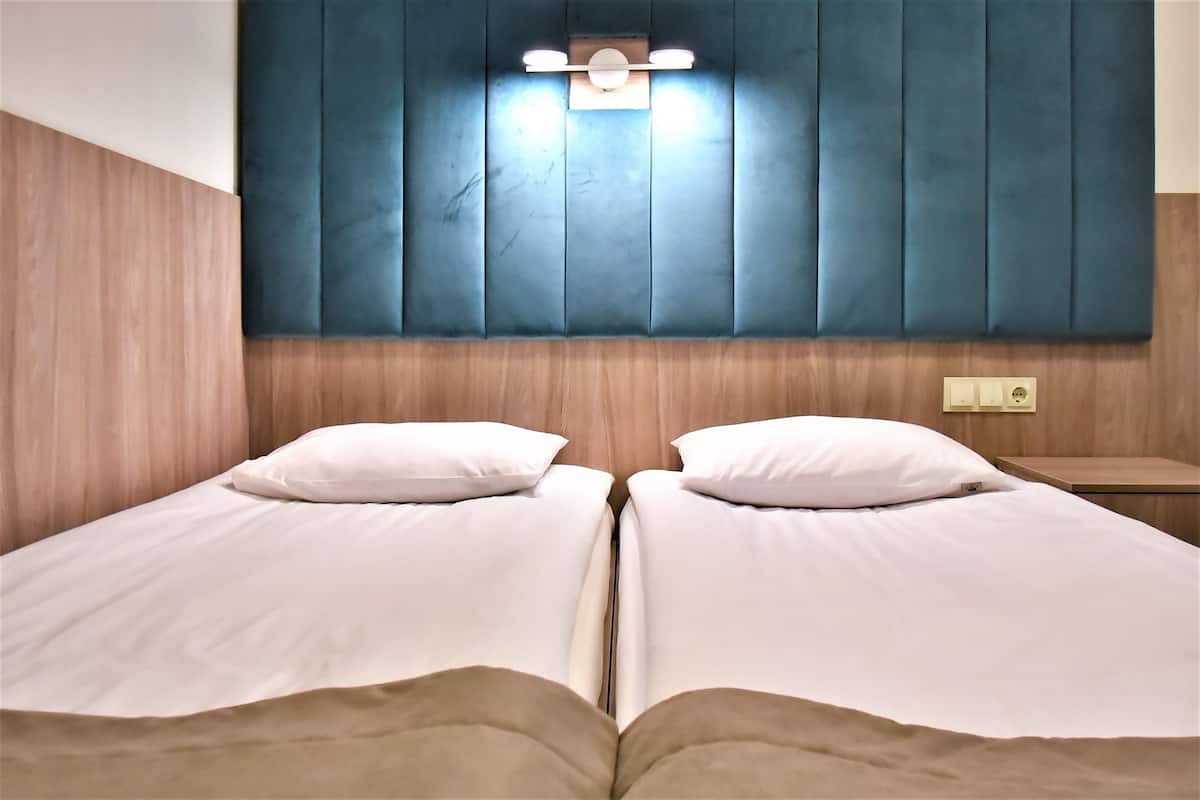 Un letto matrimoniale con biancheria da letto bianca e due cuscini, una testiera in legno e un comodino con una lampada.