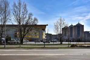 A modern building with large windows and a flat roof, surrounded by a parking lot and a fence. - EXPO Hotel Comfort (Kyiv)