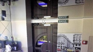 A reception area with a modern counter, a coffee machine, a door with a handle, and a wall with a cityscape mural. - EXPO Hotel Comfort (Kyiv)