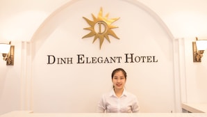 Mostrador de recepción en el Hotel Dinh Elegant, con un logotipo en la parte superior y una recepcionista.