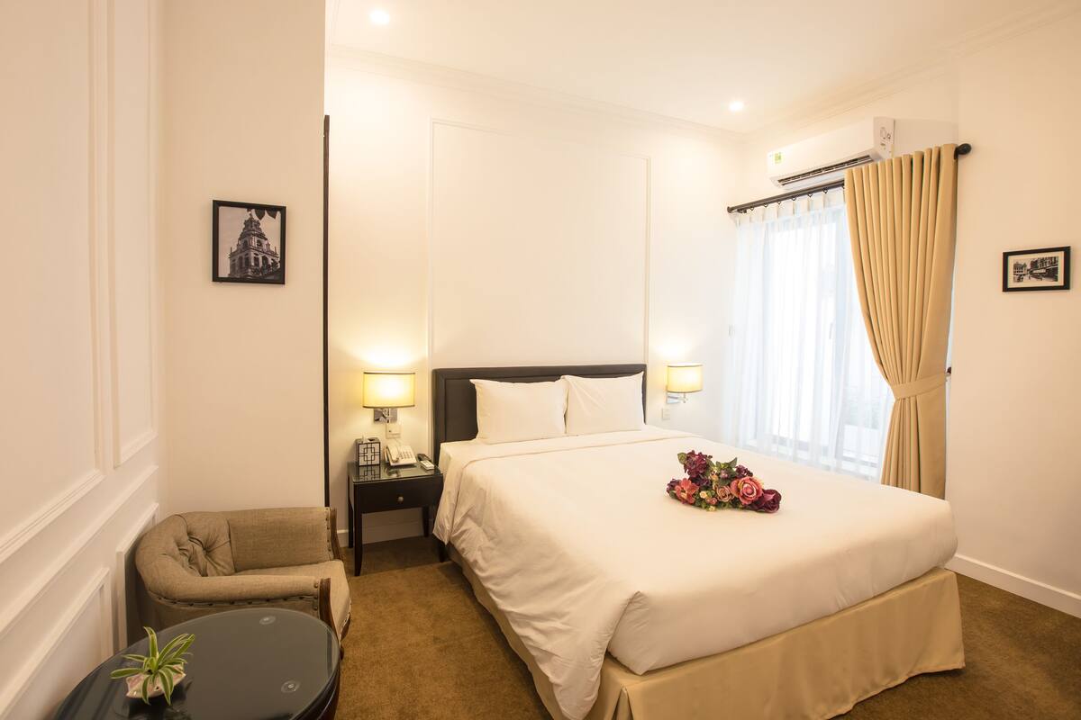 A hotel room with a large bed, bedside lamps, a small table with a plant, and a chair.