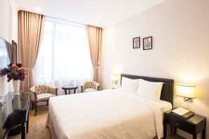 A hotel room with a large bed, two armchairs, a desk with a chair, a small table, and a nightstand with a lamp. - Dinh Elegant Hanoi Hotel (Hanoi)
